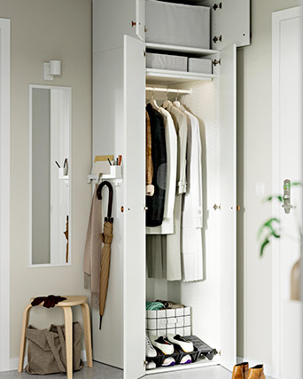 Armario alto blanco de puertas abiertas que revela ropa colgada, cajas organizadoras y zapatos, ubicado en un pasillo de tonos neutros.