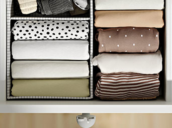 Vista superior de un cajón organizado con ropa enrollada de forma ordenada y un cepillo de pelo de color mostaza cerca.