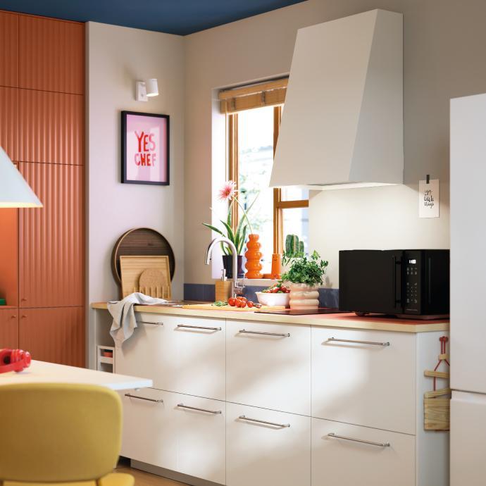 Contemporary kitchen with white cabinets, a modern range hood, wooden countertop, and colorful decor near the window.