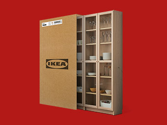 A wooden display cabinet with glass doors next to a flat IKEA cardboard box, presented against a vibrant red background.