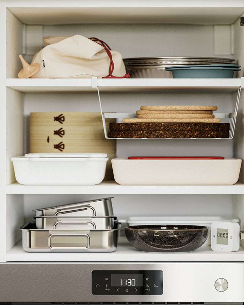 A kitchen cabinet has an open door with kitchen items stored on the shelves inside. One shelf has a PÅLYCKE clip-on basket.