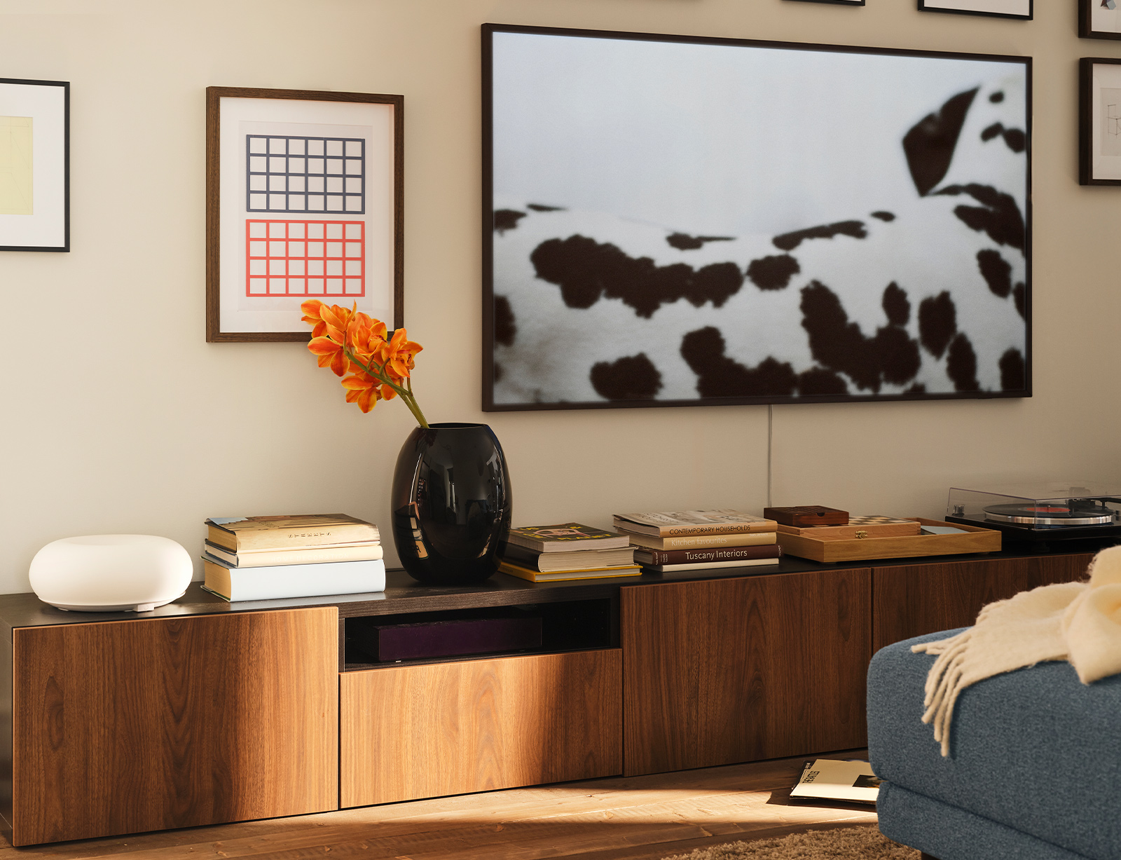 Dos bancos para TV BESTÅ están colocados contra una pared con un televisor y cuadros encima. Una lámpara LED de mesa/pared VARMBLIXT se encuentra sobre uno de los bancos.