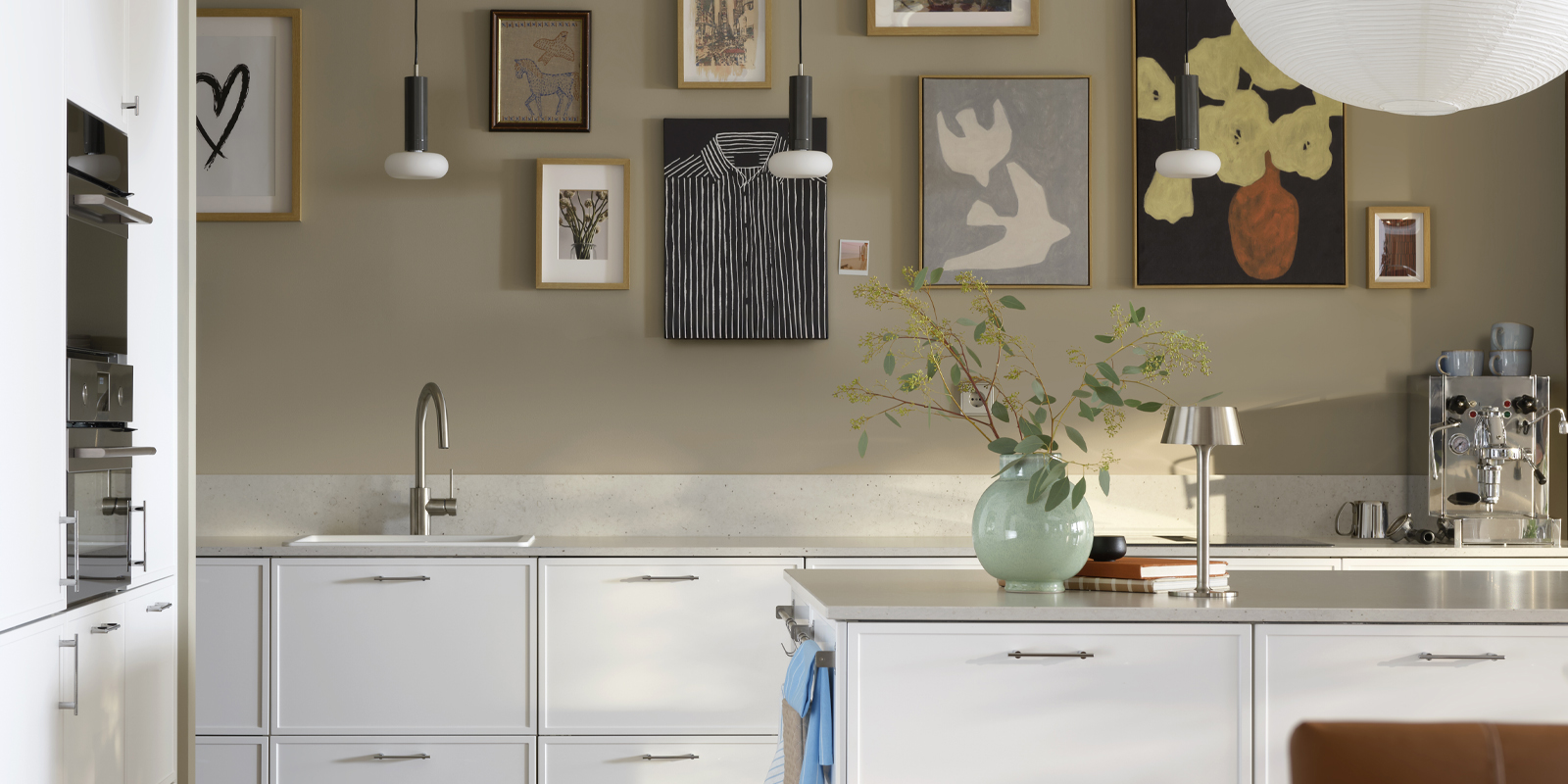 A modern Nordic-style kitchen with white cabinets, a light-colored stone countertop, a wall decorated with a gallery of paintings, and a central island with accessories.