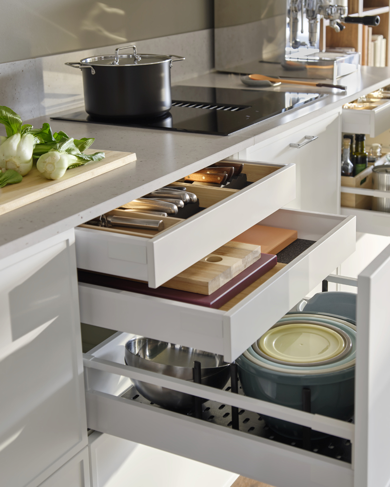 Pull-out kitchen drawers organized with interior accessories, showcasing efficient storage for utensils, cutting boards, and bowls on a modern countertop.