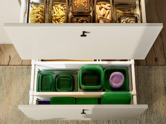 Vista superior de cajones de cocina abiertos con recipientes transparentes para pasta y tapas verdes para comida, todo ordenado y funcional.