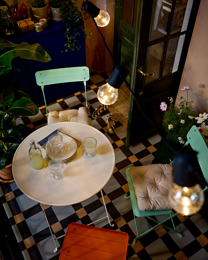 Outdoor cushion with yellow and white stripes on a wooden chair on a sunny terrace surrounded by green garden plants.