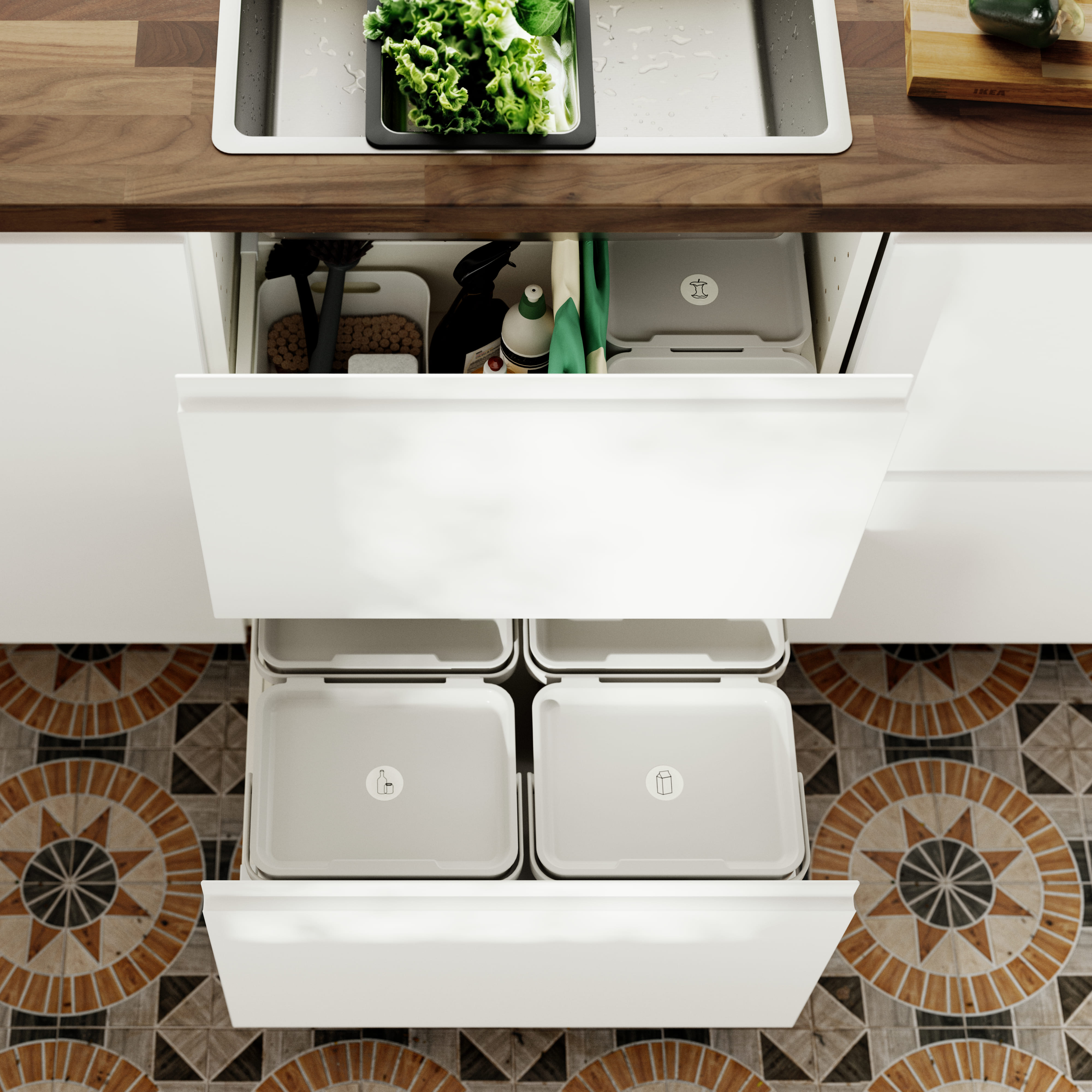 Top view of open kitchen drawers featuring labeled recycling bins, set against a decorative mosaic tile floor.