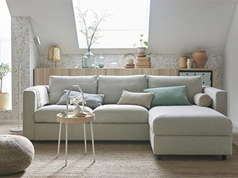 Light gray sectional sofa in a bright room with natural decor, botanical wallpaper, and a wooden side table.