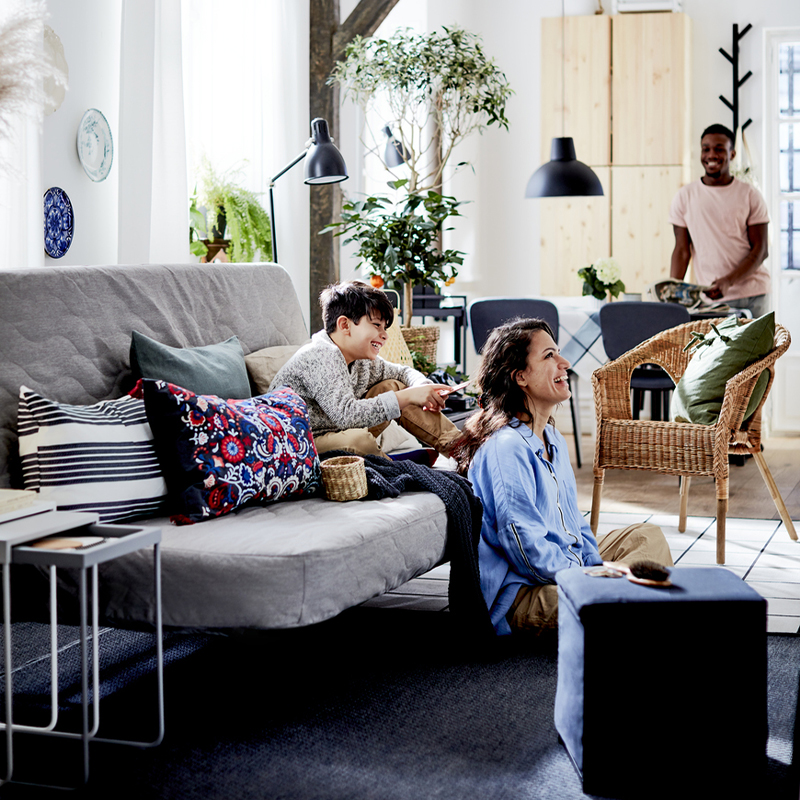 A family enjoys a happy moment in a bright, modern living room with gray sofas, indoor plants, and light wood furniture.