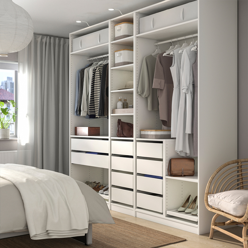 Organized open white wardrobe in a bright bedroom featuring hanging clothes, drawers, and accessory shelving.