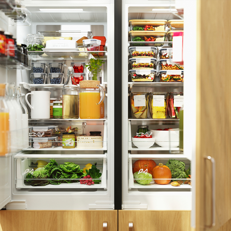 Interior of a perfectly organized refrigerator with glass containers, fresh fruits, vegetables, and juice carafes.
