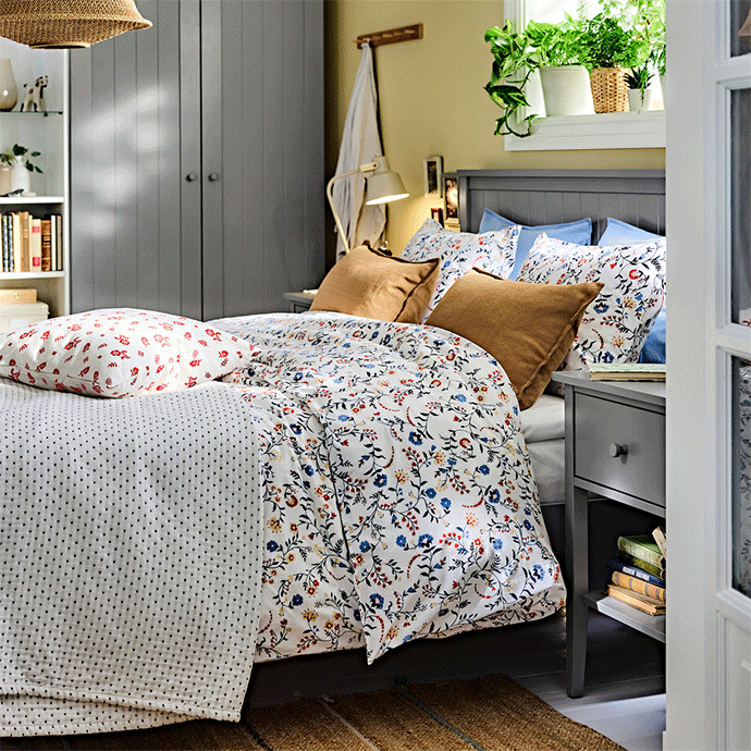 A bedroom setting with a GULLABERG bed frame, shown with pillows, a duvet cover with a floral pattern and a bedside table.