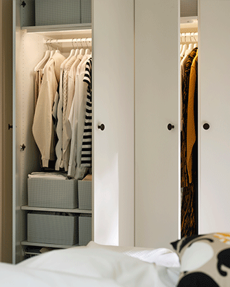 Combinación de armario LASTARE en color blanco con las puertas abiertas, mostrando ropa colgada y cajas de almacenaje en su interior.