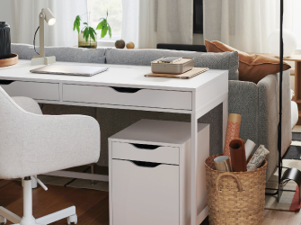 A white desk with drawers positioned behind a gray sofa, including a white chair and a matching drawer unit.