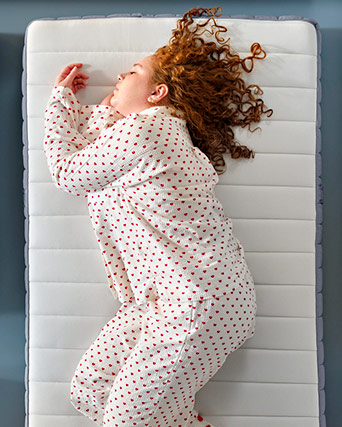 Una persona duerme cómodamente de lado sobre un colchón firme, vistiendo un pijama blanco con pequeños corazones.