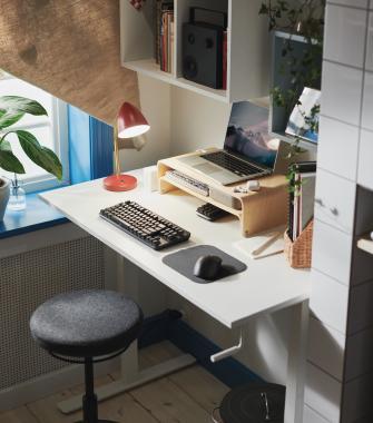 Ergonomic home workspace featuring a white standing desk, a laptop on a wooden riser, a mechanical keyboard, and a red desk lamp.