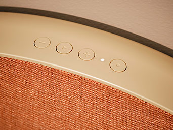 Close-up of touch control buttons on the curved top edge of a speaker featuring an orange fabric front panel.