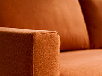 Close-up detail of a bright orange sofa's fabric and square armrest, showing a soft and textured finish.