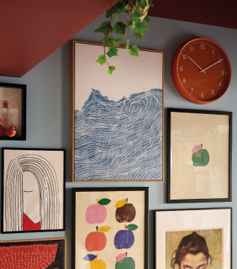 Gallery wall with framed art prints and an orange round clock on a grey wall, in a modern and creative décor setting.