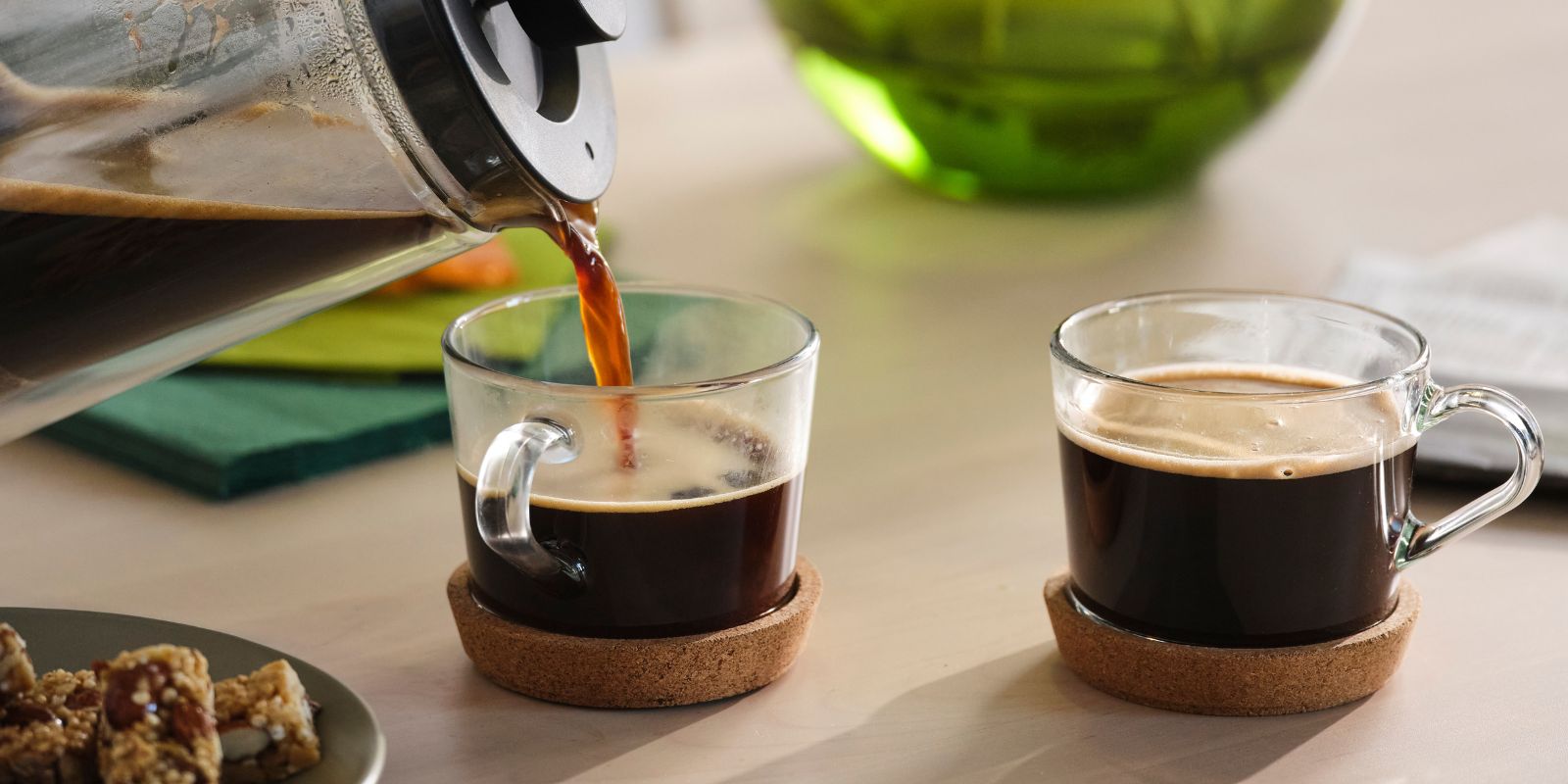 Mesa de café minimalista con taza y posavasos IKEA 365+, cafetera UPPHETTA, plato MOSSMAL y barrita de cereal.