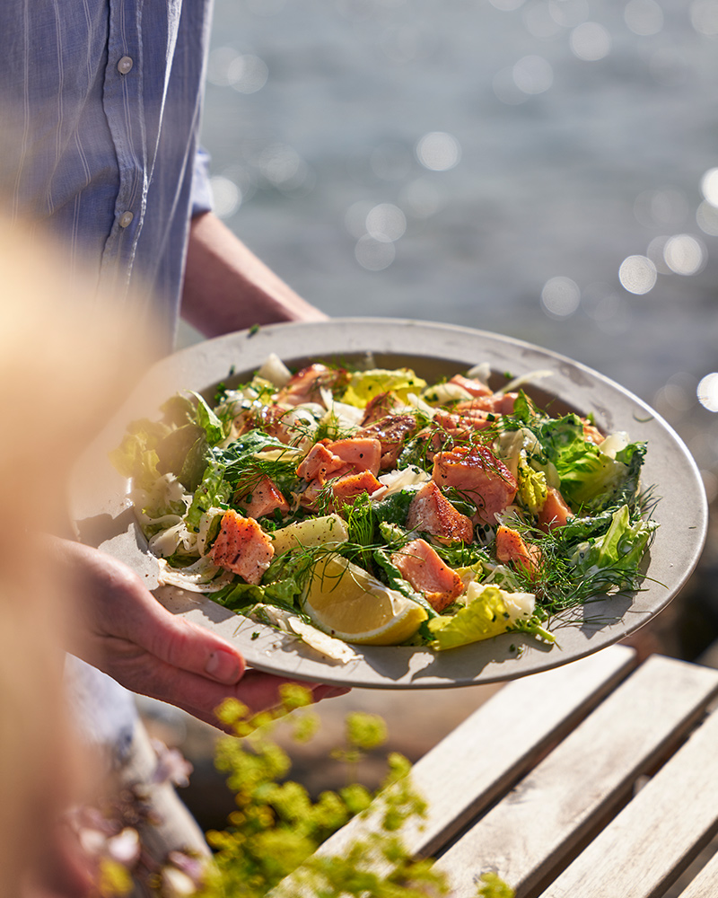 Una persona sosteniendo un plato STOCKHOLM con un plato preparado a partir de filete de salmón SJÖRAPPORT.
