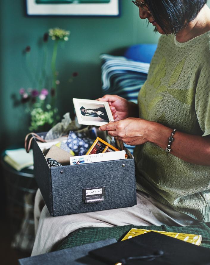 Person looking through photographs and keepsakes stored in a memory box inside a calm room.