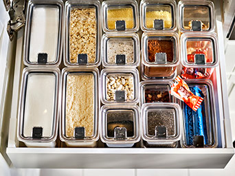 Open kitchen drawer seen from above, neatly organized with transparent food containers filled with various dry ingredients and spices.