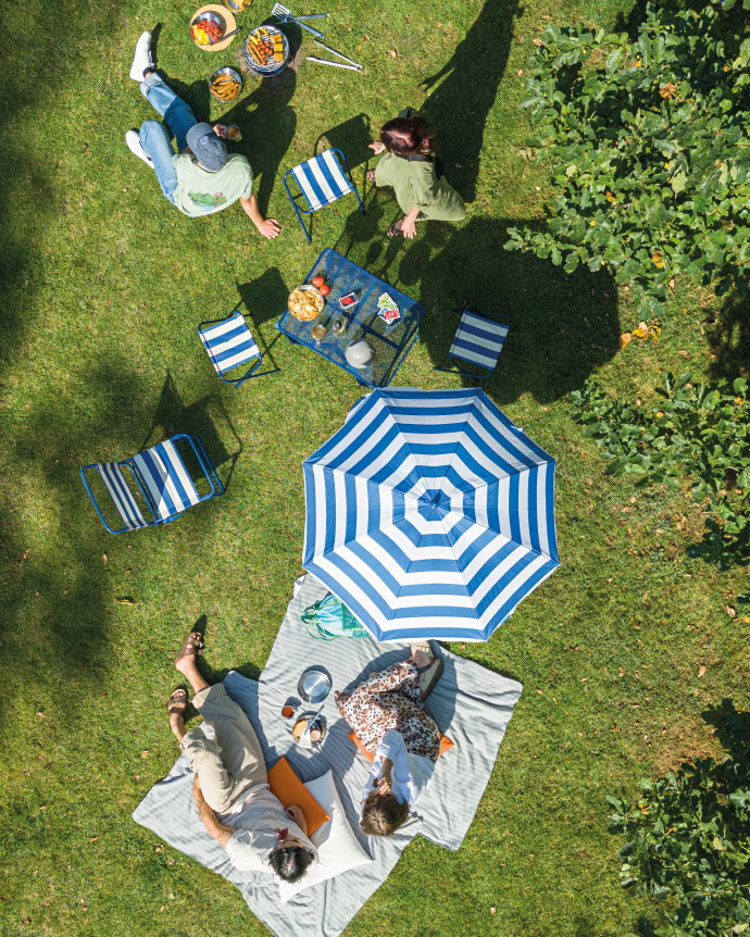 Picnic en jardín con manta, sombrilla y mesa pequeña vista desde arriba.