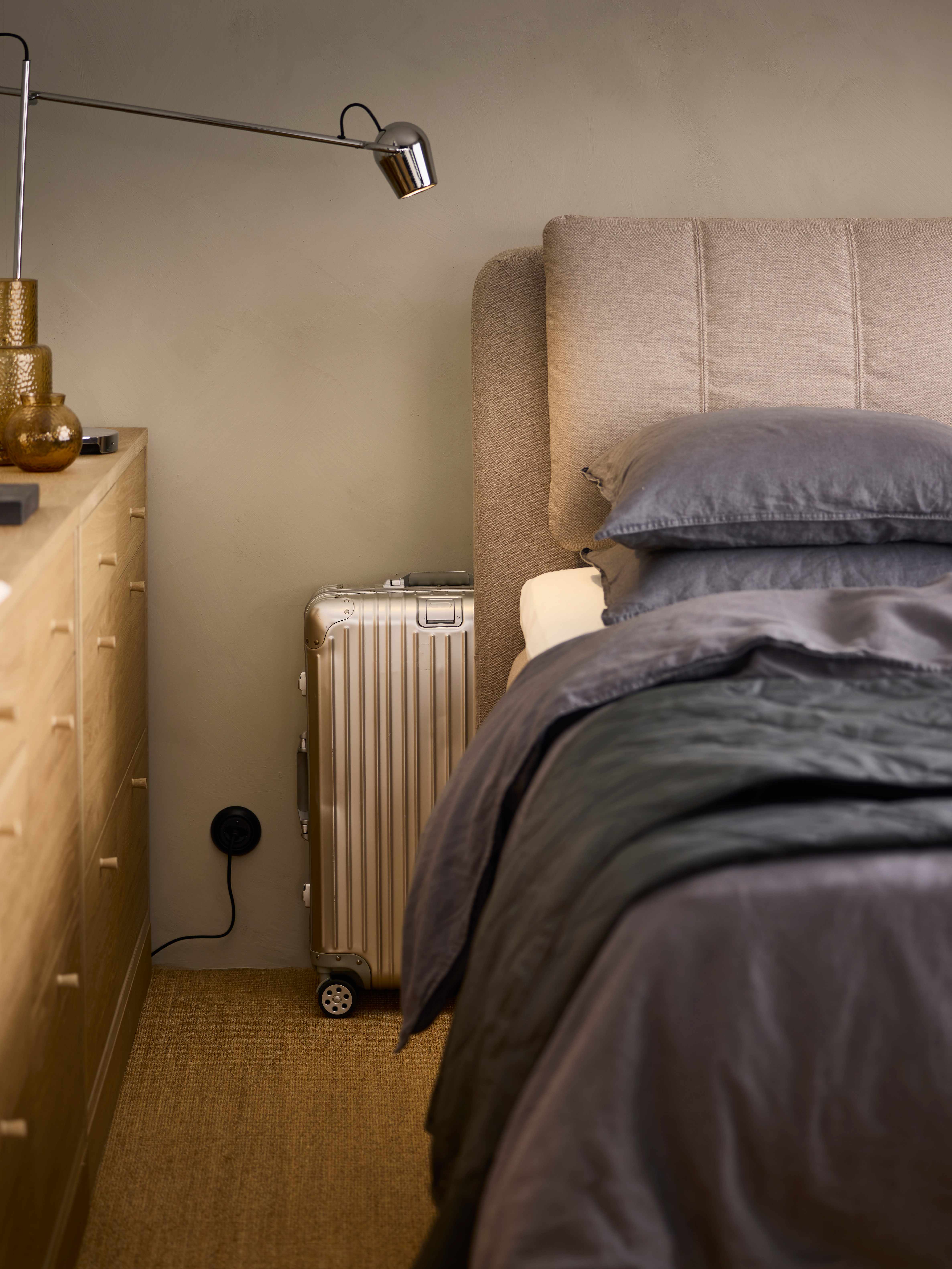 Modern bedroom with bed, lamp, and suitcase by the nightstand.