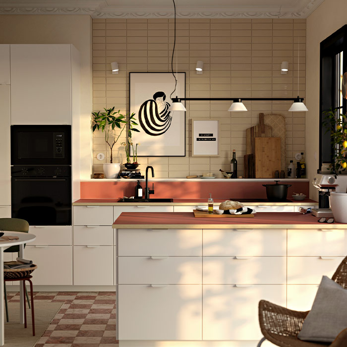 Cocina luminosa con isla blanca, encimera rojiza, azulejos beige en la pared, cuadros decorativos y una lámpara de techo moderna sobre la isla.