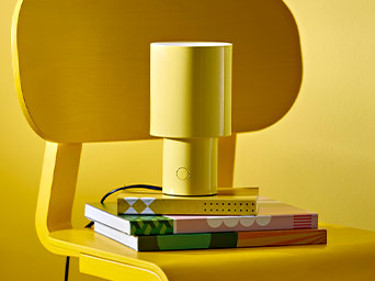 Lámpara de mesa de color amarillo sobre unos libros con patrones geométricos, colocados encima de una silla a juego.