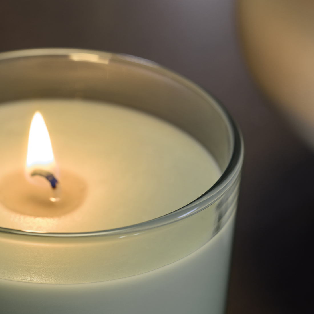 Primer plano de una vela encendida dentro de un vaso de vidrio transparente, con una iluminación suave y cálida.