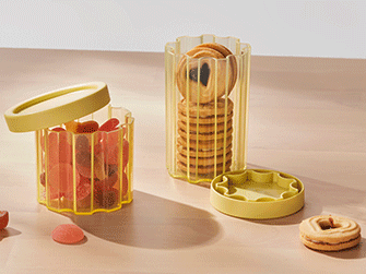 Dos botes de plástico estriado amarillo transparente con tapa sobre una superficie de madera; uno lleno de gominolas rojas y el otro con galletas redondas.