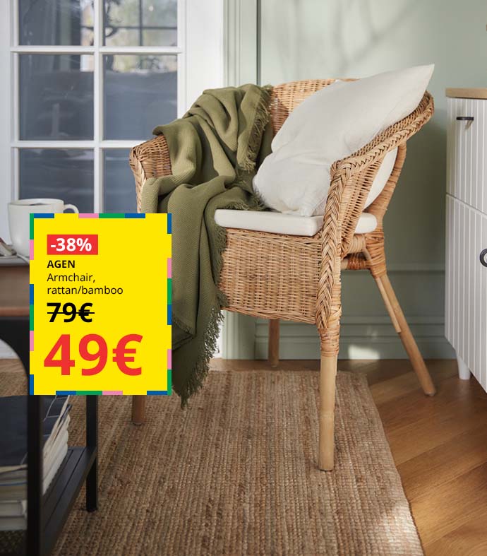 Rattan armchair with a white cushion and a green blanket, next to a side table and a white cabinet.