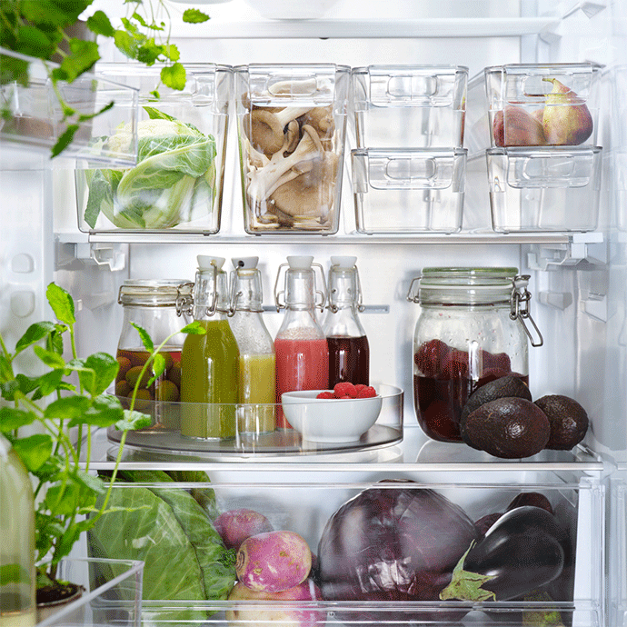 Bright, organized refrigerator interior featuring clear storage bins with fresh vegetables, flip-top glass bottles on a lazy Susan, and loose produce.