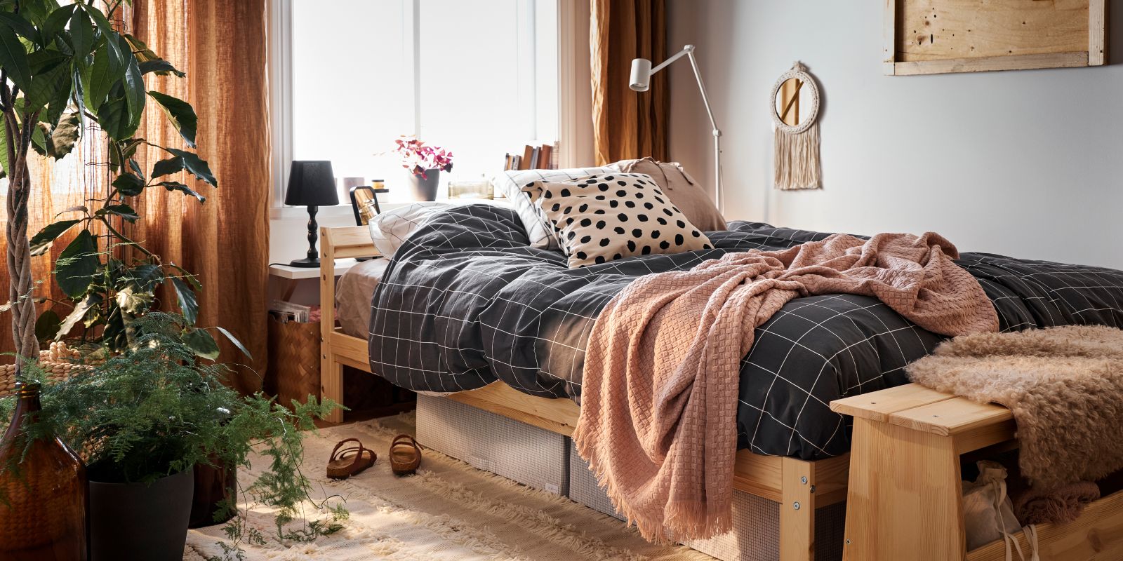 Dormitorio acogedor con cama de madera, manta rosa, luz natural y plantas que aportan calidez.