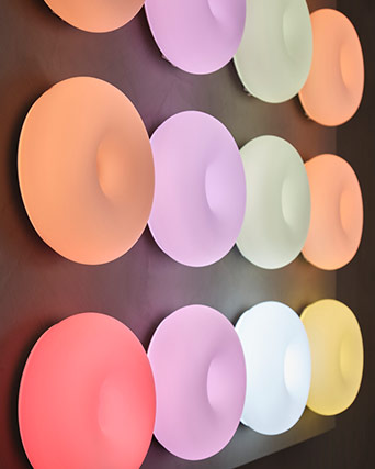 A wall display with multiple round, donut-shaped lamps glowing in various soft pastel and warm colors.