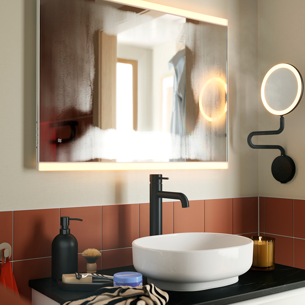Un espejo KÄRRSJÖN con iluminación integrada, montado sobre un lavabo redondo y un grifo negro, en un baño con azulejos de terracota.