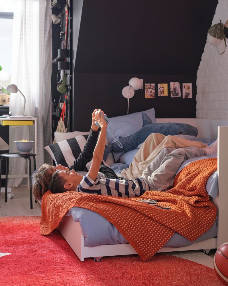 Dos adolescentes están tumbados boca arriba mirando una consola de videojuegos portátil sobre un somier VIHALS con una cama extra extensible.