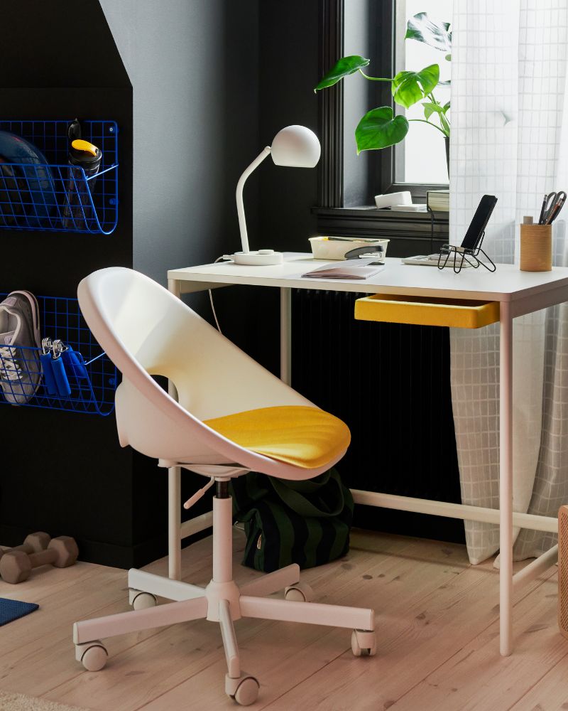  Una zona de estudio con un escritorio blanco ENKROKEN y una silla blanca LOBERGET. Hay una planta sobre el escritorio, junto a unas estanterías que hay en una pared oscura.