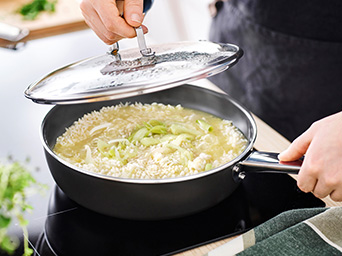 Una persona cocina arroz con verduras en una sartén antiadherente sobre una placa de inducción