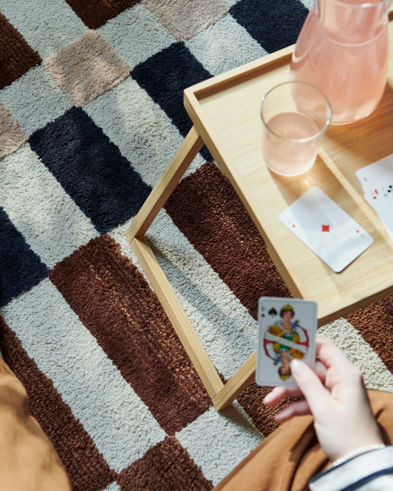Rincón relajado con alfombra MARKBLÅMME, bandeja de cama RESGODS, jarra KARAFF y vaso STOCKHOLM 2025.