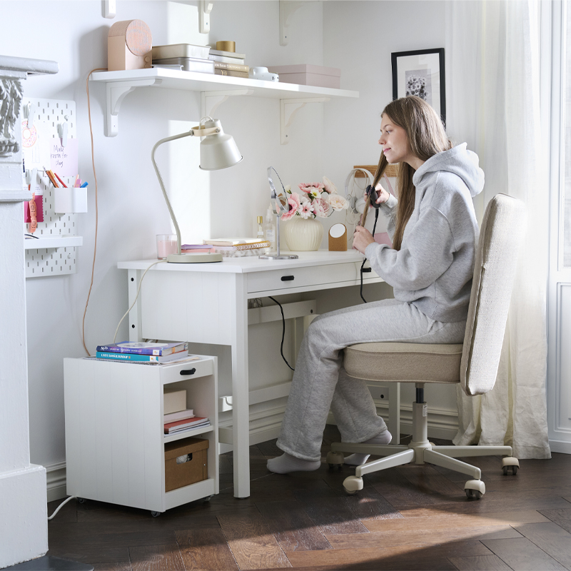 A workspace with a white BRYTNING desk made from wood is being used by a person in a grey outfit.