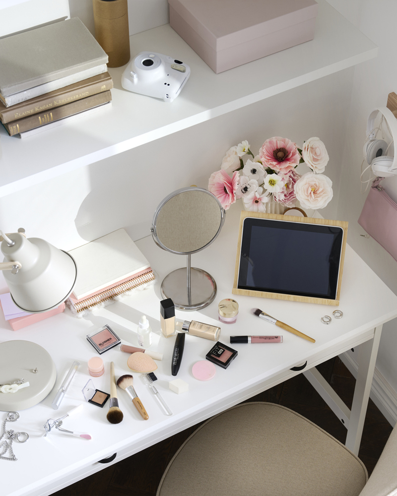 A bedroom with a white BRYTNING desk made from white material. It holds cosmetics and a mirror on top.