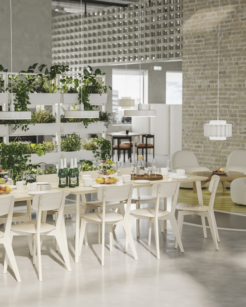 Un comedor de oficina muy luminoso, con mesas blancas y sillas de madera, flanqueado por maceteros con plantas que cuelgan en cascada.