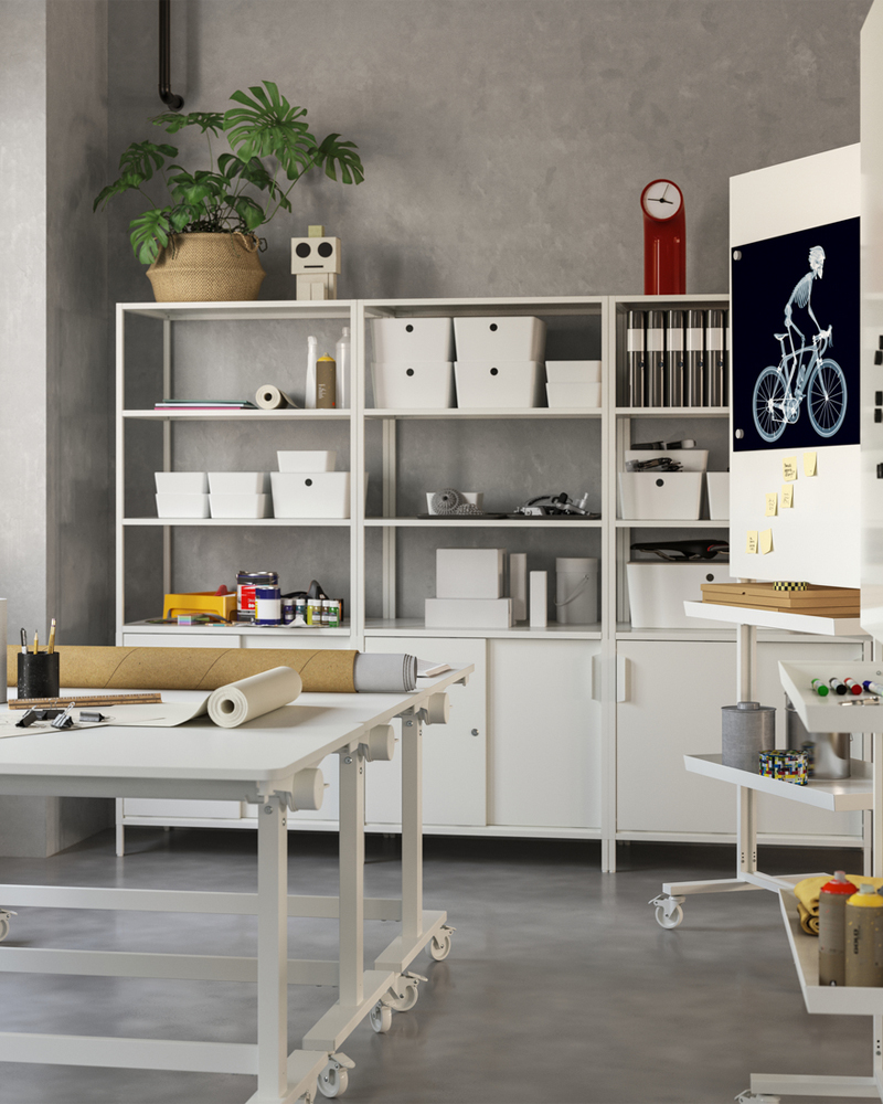 Espacio de trabajo creativo con dos mesas blancas con ruedas. Muebles de almacenamiento con compartimentos cerrados y abiertos apoyados contra la pared del fondo.
