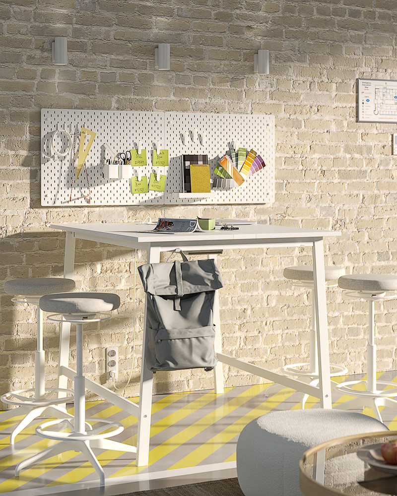 Mesa alta blanca con cuatro taburetes altos, situada frente a una pared de ladrillo claro con un panel perforado que contiene materiales artísticos.