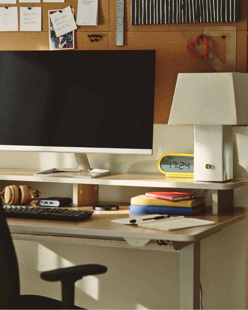 A home office with a beige TRAVSPORT desk sit/stand made from electric oak effect, featuring a computer and stationery.