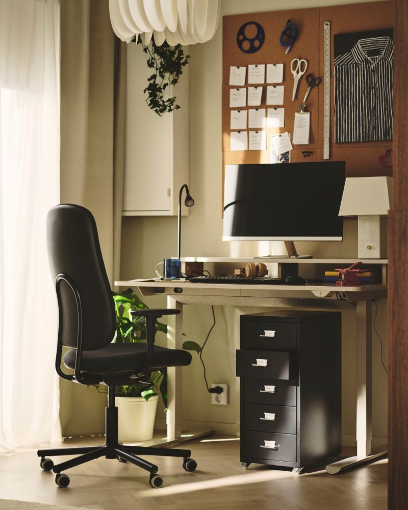 A home office with a beige TRAVSPORT desk sit/stand made from electric oak effect, featuring a computer and stationery.