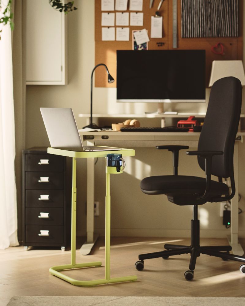 Laptop stand next to a dark grey SMÖRKULL office chair with armrests beside a desk and plants by the wall.
